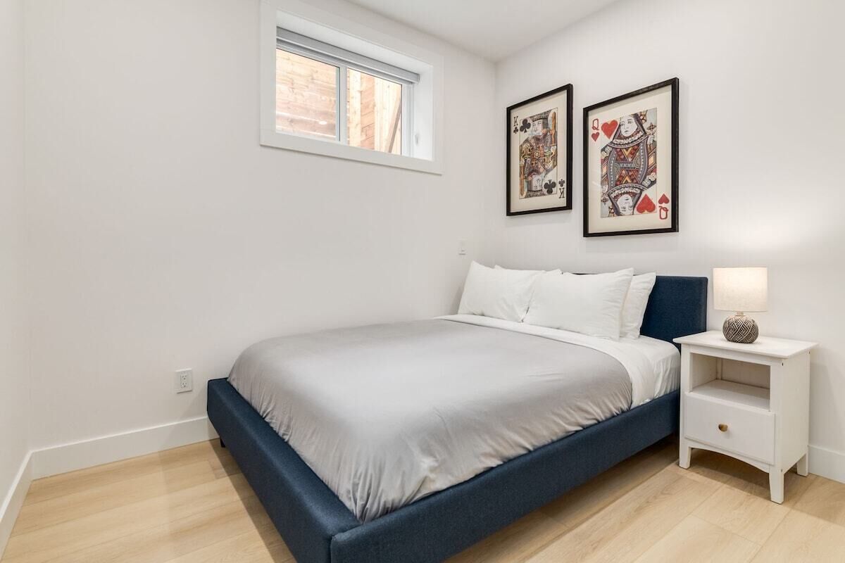 A bedroom with a bed, a nightstand, a window, and two framed pictures on the wall.