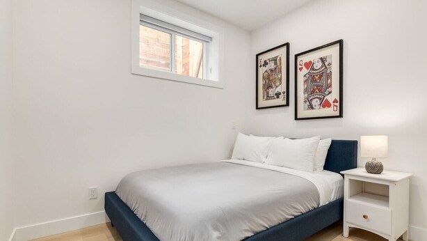 Un dormitorio con cama, mesita de noche, ventana y dos cuadros en la pared.