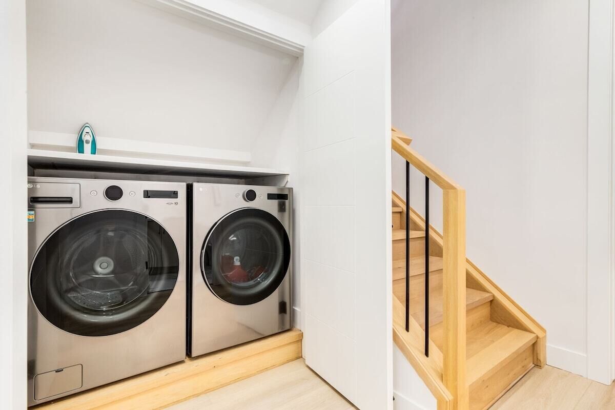 A laundry area with two stainless steel washing machines and a wooden staircase.