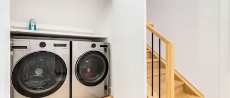 A laundry area with two stainless steel washing machines and a wooden staircase.