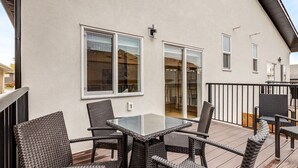 A balcony with wicker furniture and a glass table, a white building exterior, and a black railing. - Brand New Perfect Family Home, w/ Garage Parking (Calgary)