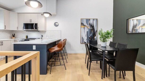 A modern kitchen with a central island, bar stools, and a dining area with black chairs and a table. - Brand New Perfect Family Home, w/ Garage Parking (Calgary)
