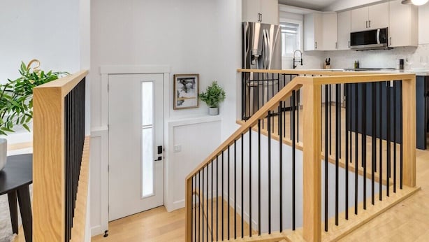 A modern kitchen with white cabinets, stainless steel appliances, and a wooden staircase with black railings.