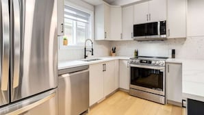 A modern kitchen with stainless steel appliances, white cabinetry, and a herringbone-patterned backsplash.