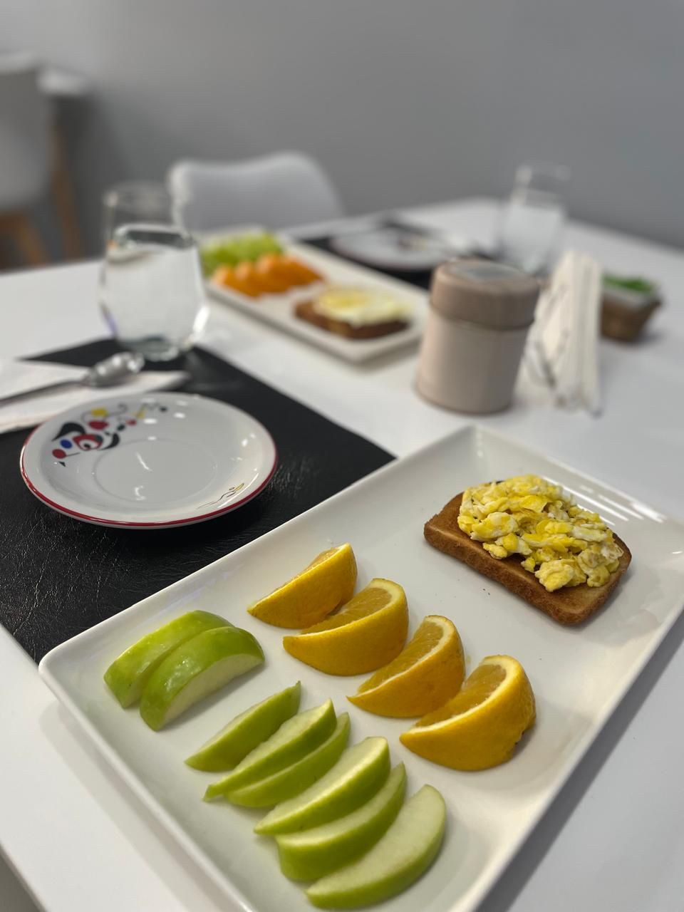 A breakfast setting with toast, scrambled eggs, and sliced apples and lemons on a white plate.