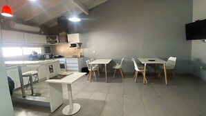 A modern kitchen with white cabinets, a microwave, and a dining area with white chairs and tables. - Gugasuites (Ezeiza)