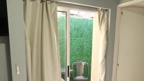 A hotel room with a bed, a sliding glass door leading to an outdoor area with a chair and a green hedge. - Gugasuites (Ezeiza)