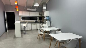 A modern kitchen with white cabinets, a microwave, and a water dispenser. There are white chairs and a table in the dining area. - Gugasuites (Ezeiza)