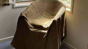 Ein Zimmer mit einem großen Fenster, einem Sessel mit beigebezogenem Bezug und Blick auf Grünfläche.