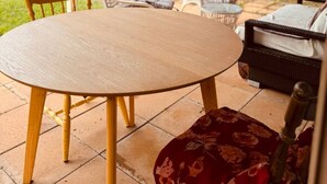 Eine überdachte Terrasse mit einem runden Holztisch und Stühlen, einem Rattansofa und einer Treppe, die zu einer oberen Ebene führt.