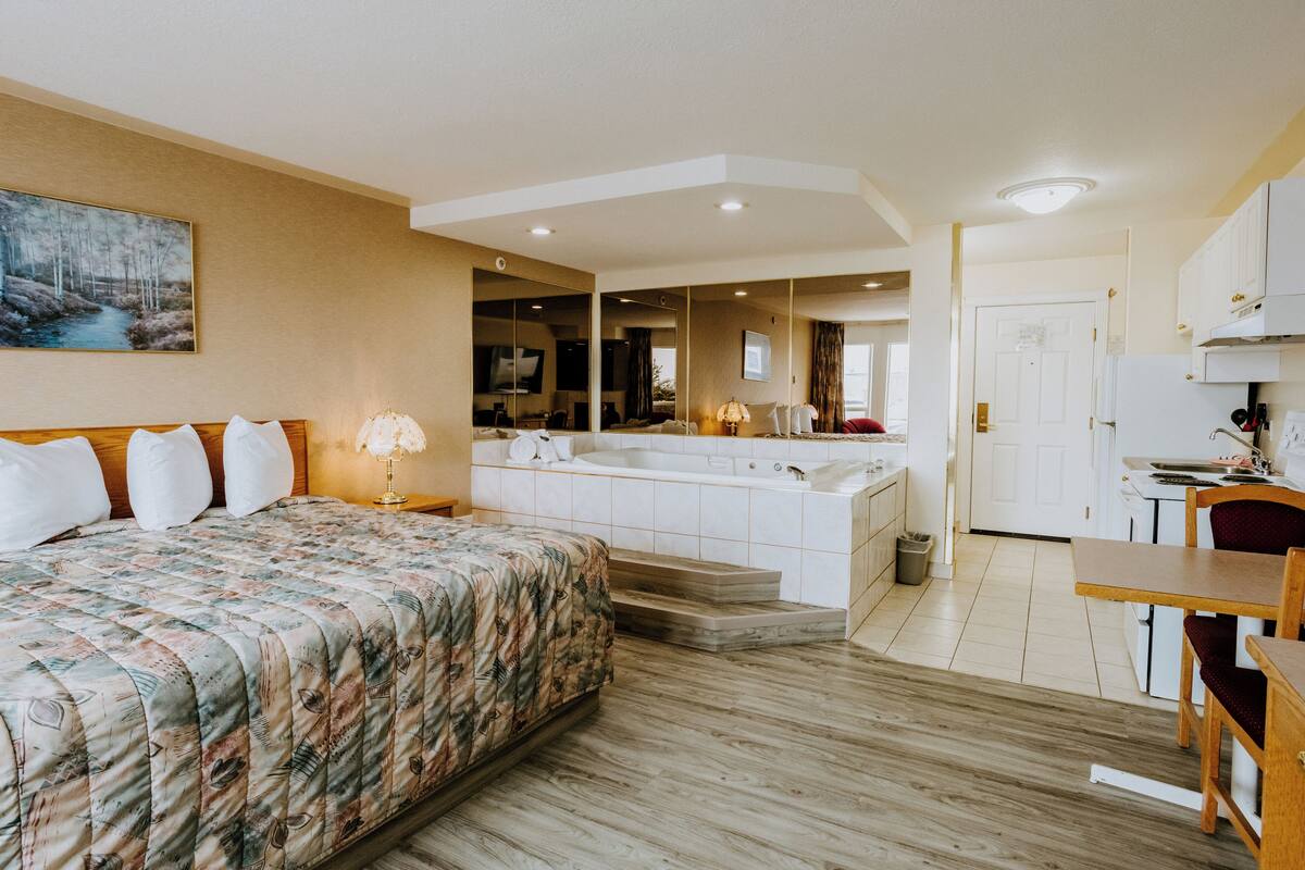 A hotel room with a bed, a desk, a kitchen area, and a bathroom.