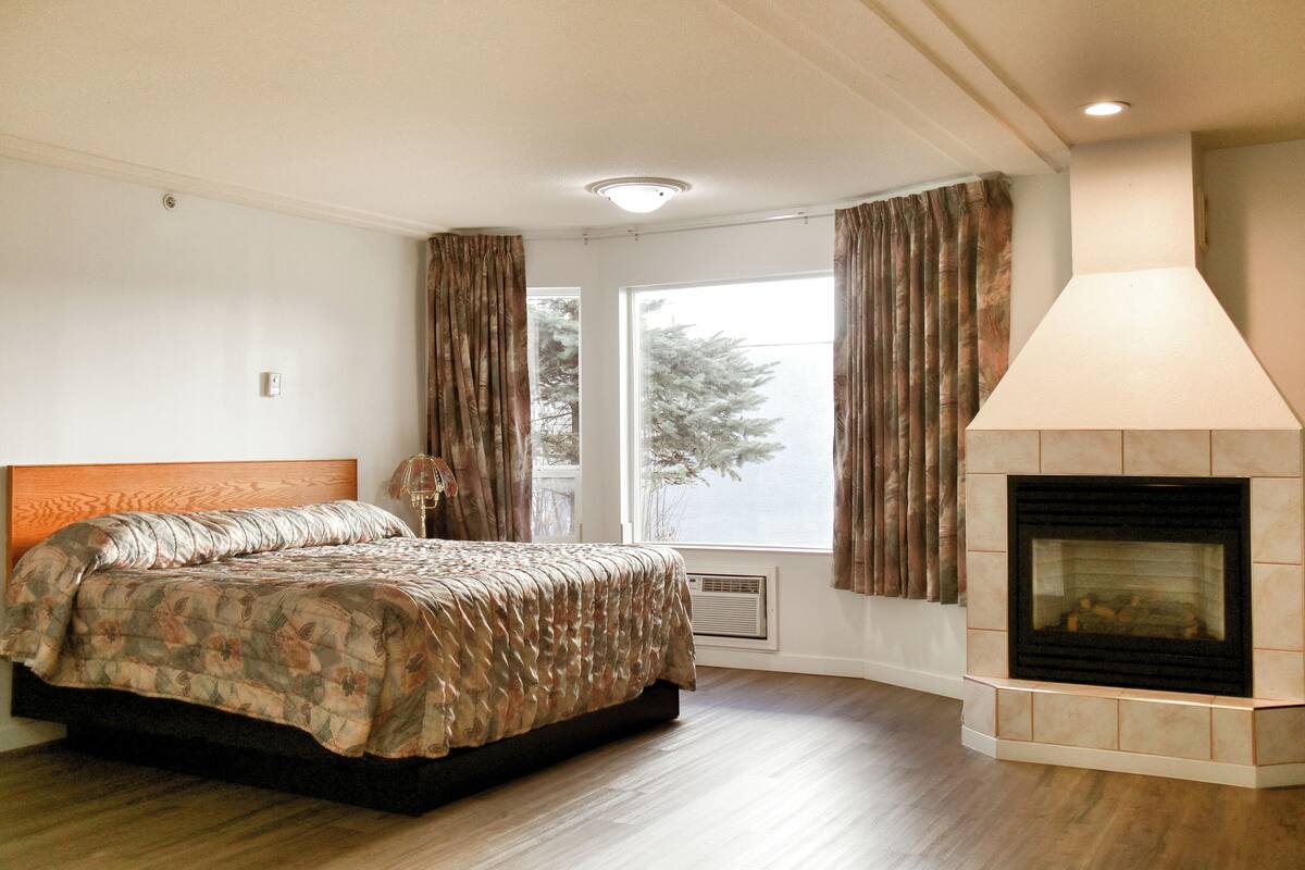 A bedroom with a bed, a fireplace, and a large window with curtains.