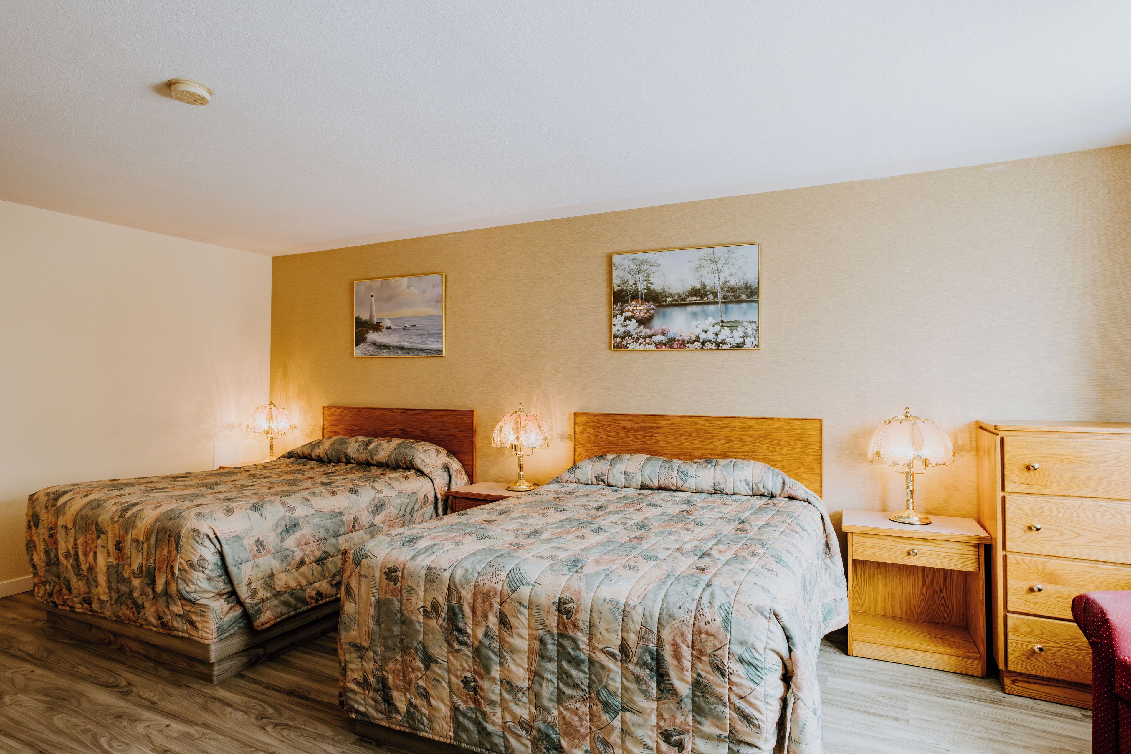 Habitación de hotel con dos camas, cabeceros de madera, mesitas de noche con lámparas y un aparador de madera.