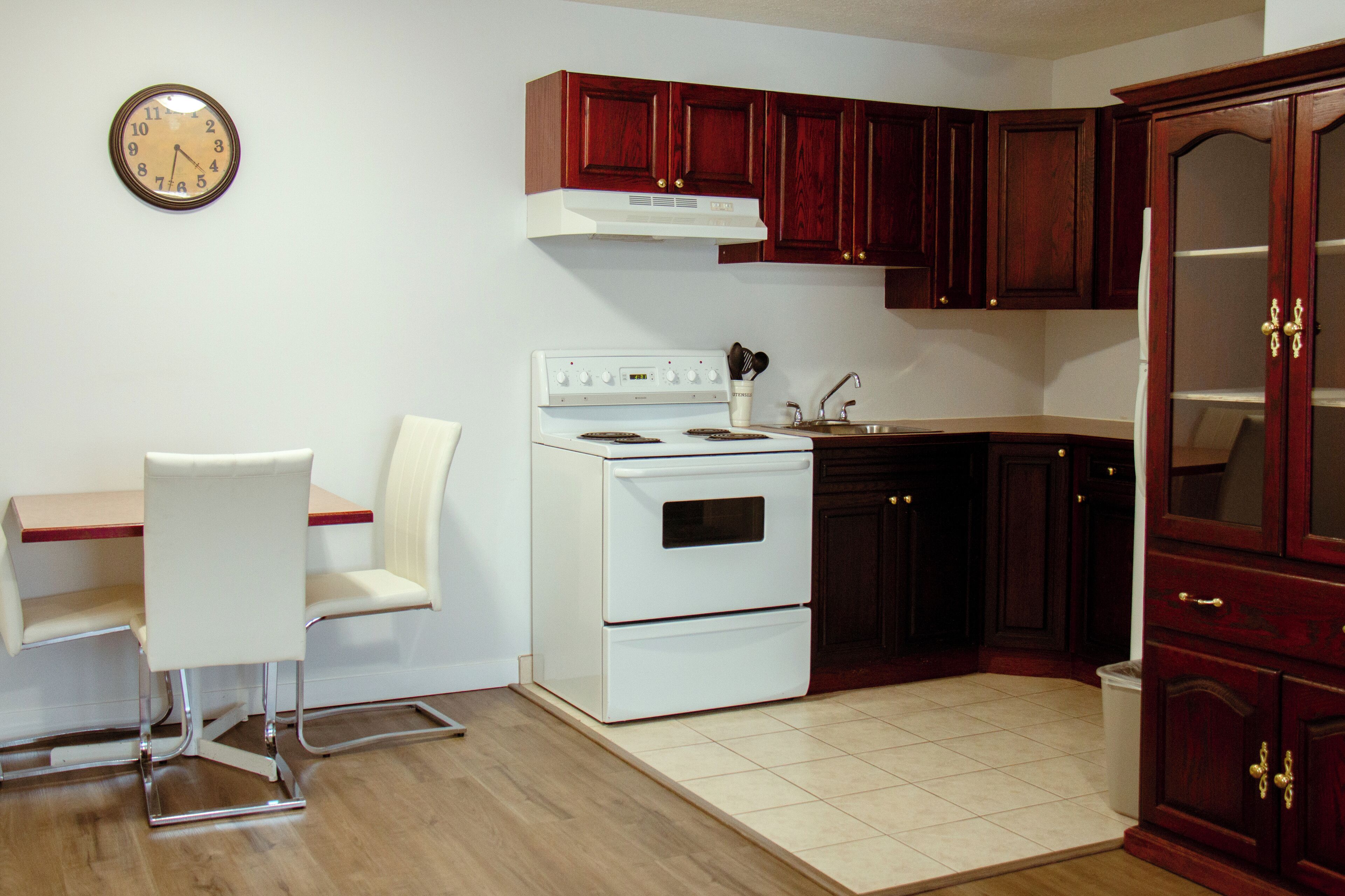 A compact kitchen with a white stove, a dining table with two chairs, and wooden cabinets.