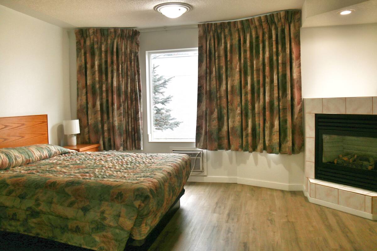 A bedroom with a bed, a fireplace, and a window with curtains.
