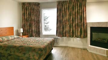 A bedroom with a bed, a fireplace, and a window with curtains.