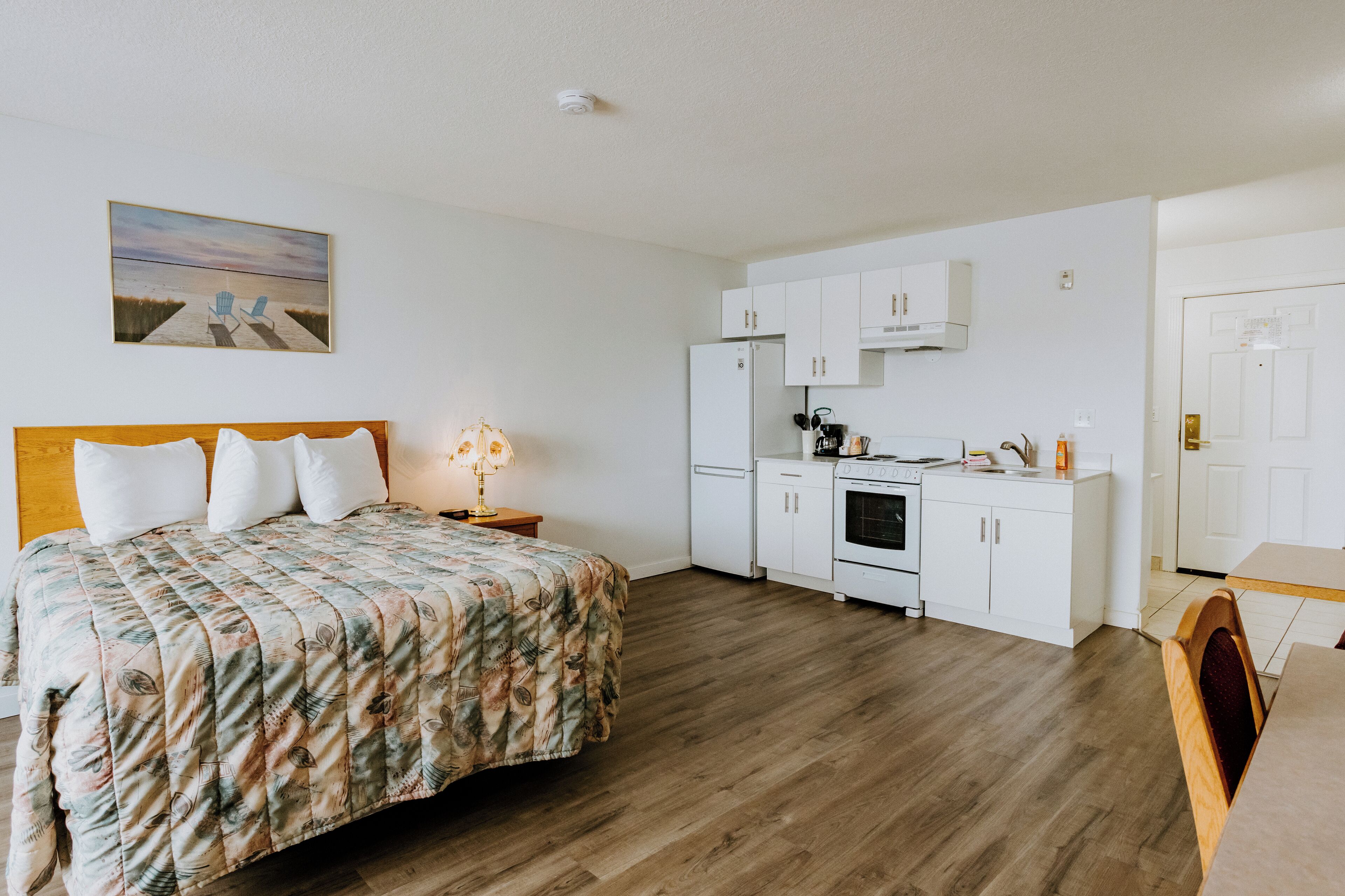 Une chambre à coucher avec un lit, une table de chevet, une lampe et un tableau représentant une scène de plage.