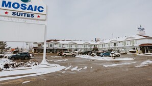 Hotel Mosaic Suites con un letrero, estacionamiento cubierto de nieve y varios coches aparcados en la entrada.