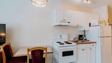 Cocina pequeña con gabinetes blancos, estufa, microondas y refrigerador. Hay una mesa de comedor con dos sillas.
