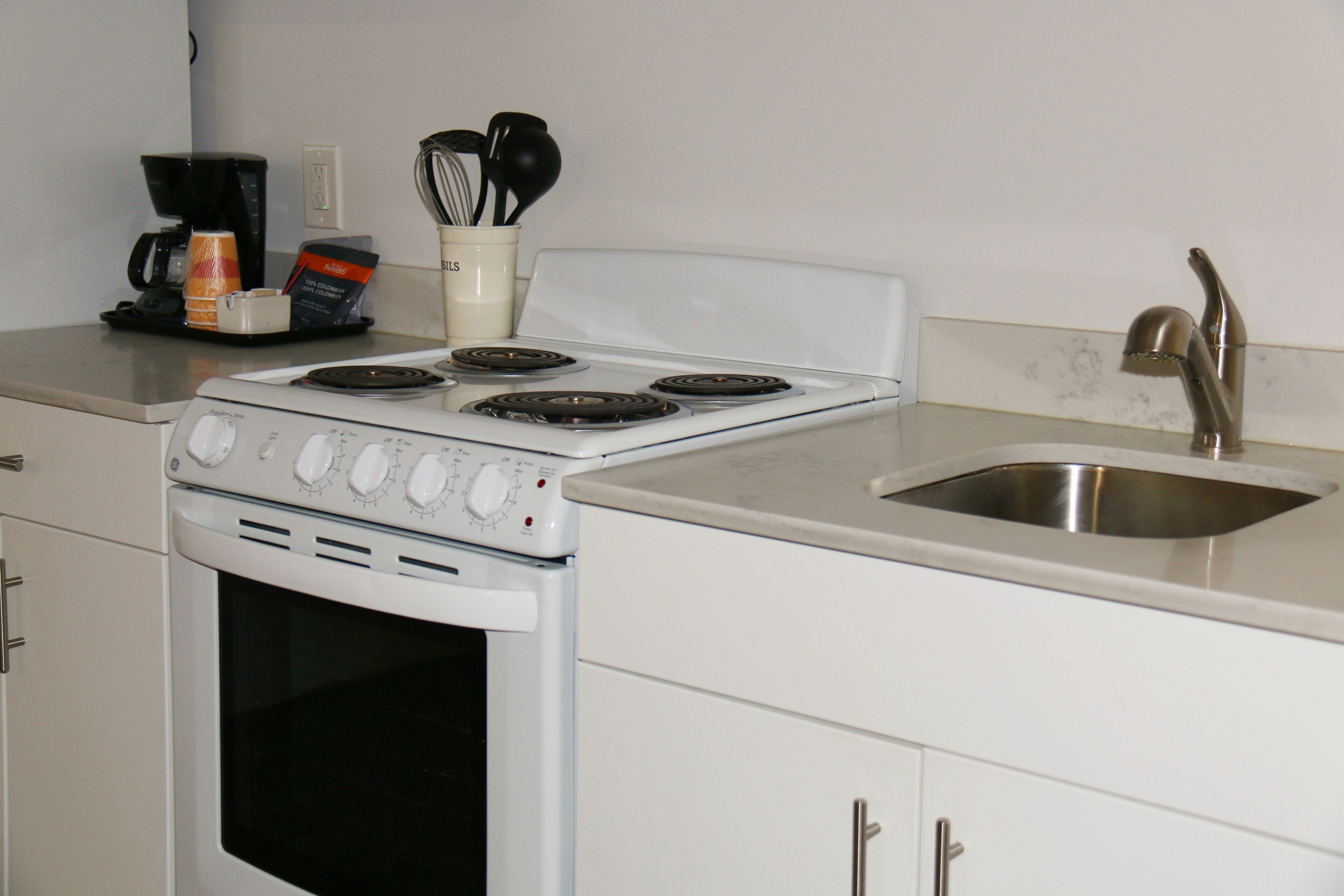 A kitchen with a white stove, a sink, and cabinets.