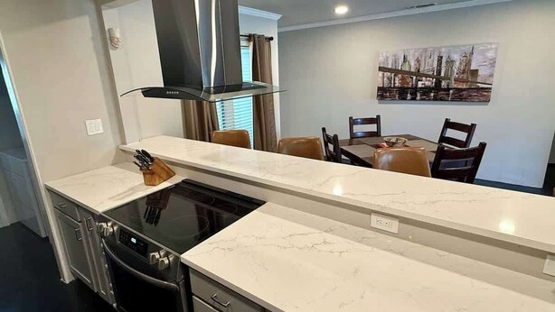 A modern kitchen with a marble countertop, black appliances, and a dining area with chairs and a table. - Hot Tub | 2BR Duplex | Pet Friendly| Near Airport (San Antonio)
