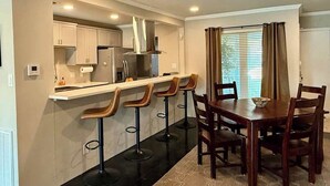 A modern kitchen with a bar area, wooden chairs, and a dining table. - Hot Tub | 2BR Duplex | Pet Friendly| Near Airport (San Antonio)