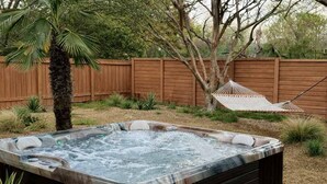 A hot tub with a wooden deck, a hammock, and a wooden fence in the background. - Hot Tub | 2BR Duplex | Pet Friendly| Near Airport (San Antonio)