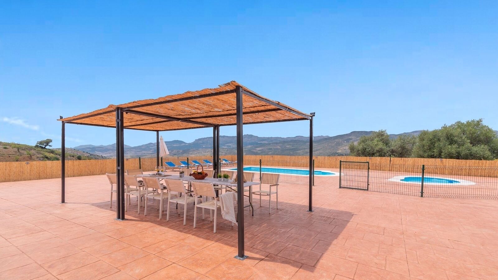 Área de estar coberta ao ar livre, com piscina e montanhas ao fundo.
