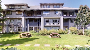 A multi-story building with a balcony on each floor, a well-maintained lawn with two picnic tables, and a variety of shrubs and plants.