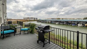 A deck with a grill, seating, and a view of a marina with boats and a bridge. - Lakefront, Boating + Private Deck - Marina Views (Rowlett)