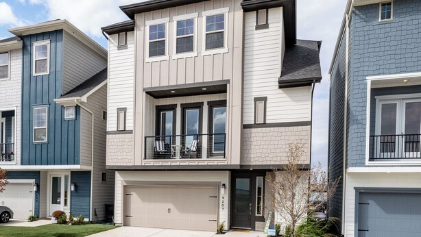 A modern two-story townhouse with a garage, a balcony with outdoor seating, and a well-maintained lawn.