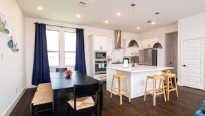 A modern kitchen with white cabinets, a central island with bar stools, and a dining area with a black table and chairs.
