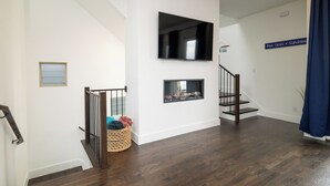A modern living room with a flat-screen TV, a fireplace, and a staircase.