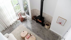 Een gezellige woonkamer met een open haard, een bank en twee houten bijzettafeltjes.