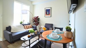 Una sala de estar con un sofá, una mesa de centro y una mesa de comedor dispuesta con platos y vasos. Hay una planta sobre la mesa de centro y otra sobre la mesa de comedor.