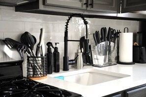 Uma cozinha com exaustor de aço inoxidável, pia com torneira preta, e diversos utensílios e eletrodomésticos organizados sobre o balcão.