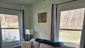 Un salon avec un canapé beige, deux coussins, une lampe et un tableau accroché au mur.