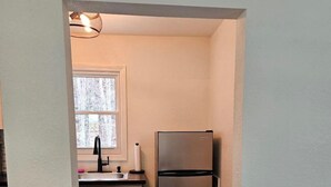 Une cuisine de taille réduite, dotée d’un réfrigérateur en acier inoxydable, d’une fenêtre au-dessus de l’évier et d’un plancher en bois.