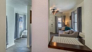 Un couloir mène à un salon équipé d’un ventilateur de plafond, d’un canapé et d’une table basse.