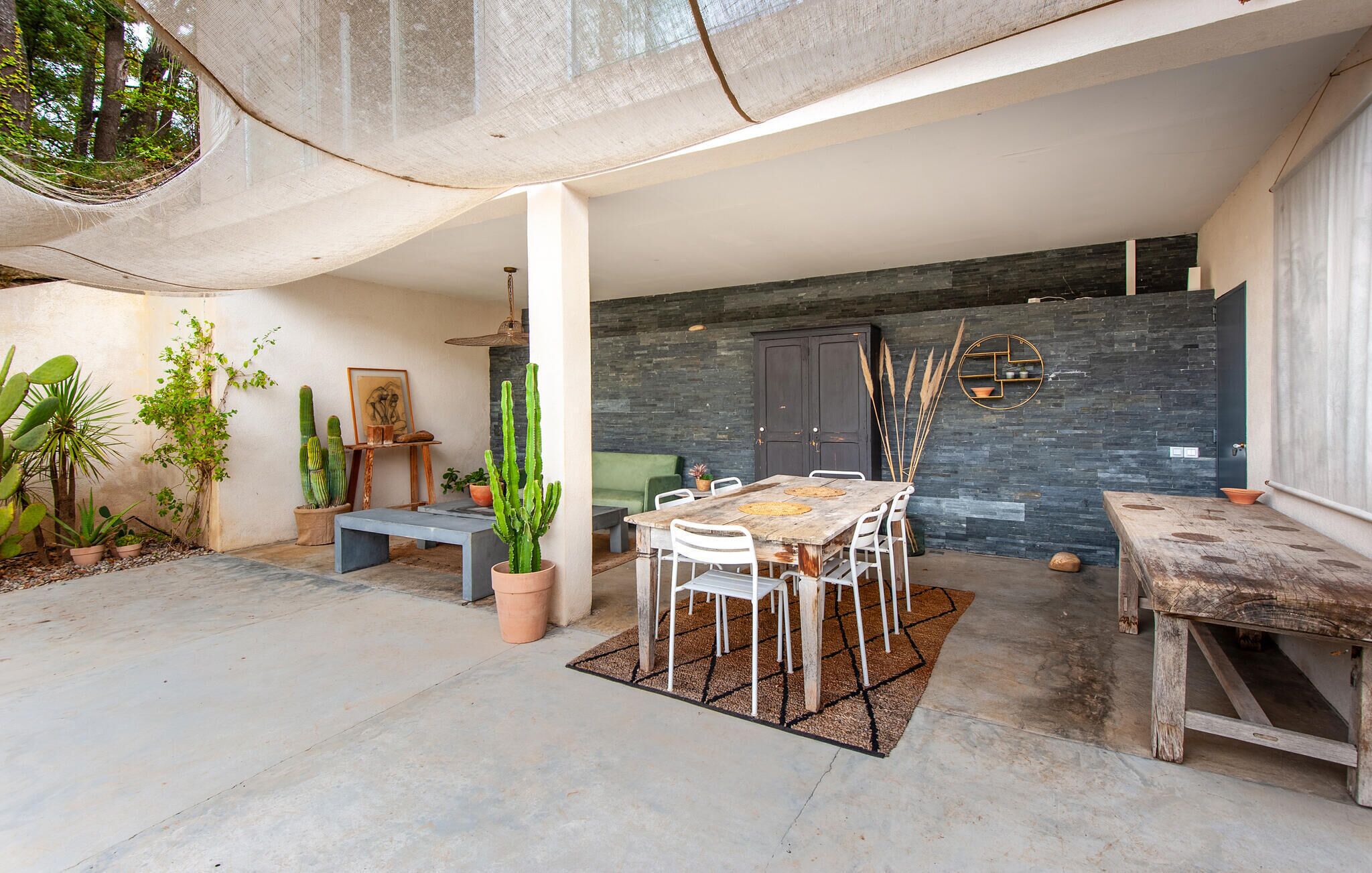 Un espace extérieur aménagé en patio, avec une table et des chaises pour les repas, entouré de plantes en pot et d’un banc en bois rustique.