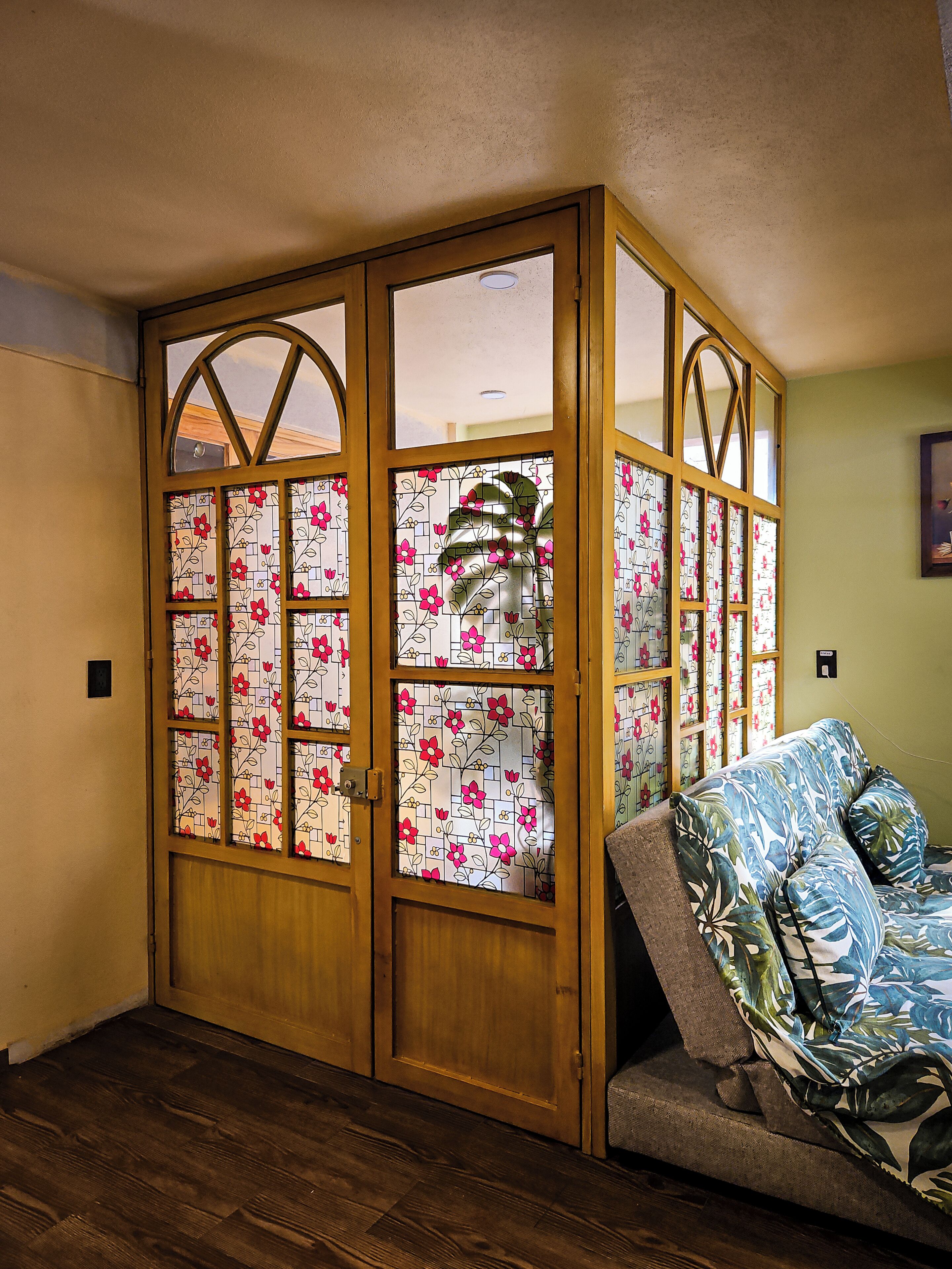 A room with a wooden wardrobe, a floral-patterned sofa, and a wall-mounted picture.