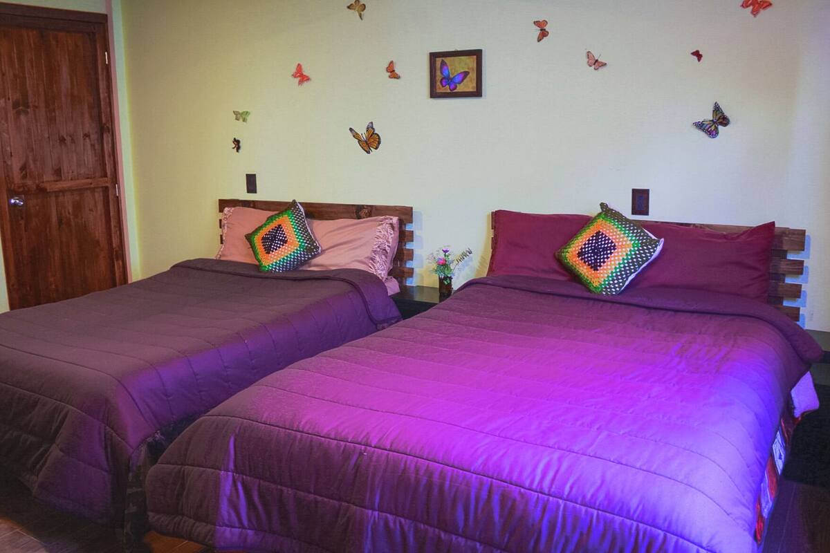 Dos camas con ropa de cama morada, adhesivos de mariposas en la pared y una puerta de madera.