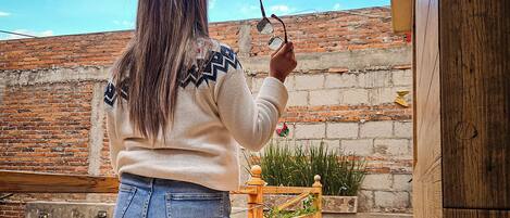 Una persona de pie sobre un área empedrada, con un muro de ladrillo y una cerca de madera al fondo.