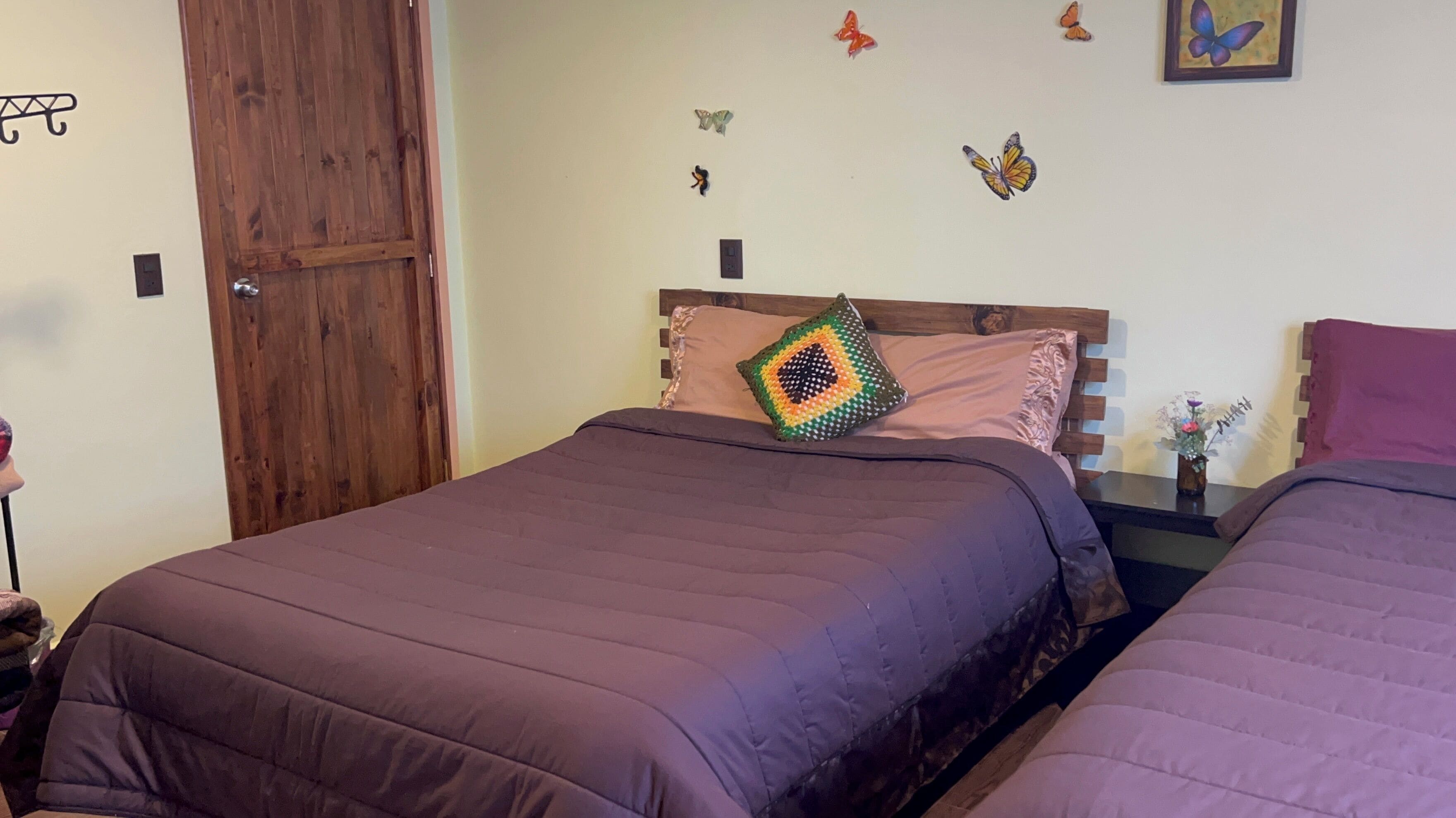 A bedroom with two beds, wooden headboards, a wooden door, and butterfly wall decals.