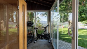 Een kamer met een houten plafond, een glazen deur naar een balkon en fitnessapparatuur.