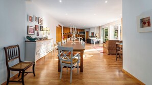 Een ruime eethoek met een lange houten tafel en stoelen, een kroonluchter en een keuken op de achtergrond.