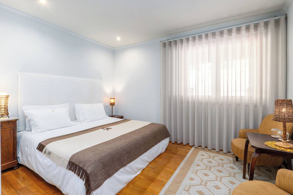 A hotel room with a large bed, a wooden floor, a desk with a lamp, and a chair.