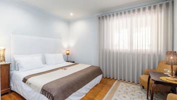 Ein Hotelzimmer mit einem großen Bett, Holzboden, einem Schreibtisch mit Lampe und einem Sessel.