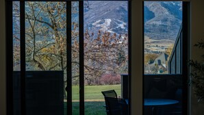 A room with a large window overlooking a mountainous landscape, a dining area with a table and chairs, and a view of a grassy area with trees. - Alpine Retreat Pt A106 | Ski Escape | Mtn Views (Eden)