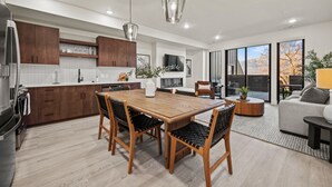 A modern kitchen with wooden cabinets, a dining table with chairs, and a large window offering a view of the outdoors. - Alpine Retreat Pt A106 | Ski Escape | Mtn Views (Eden)